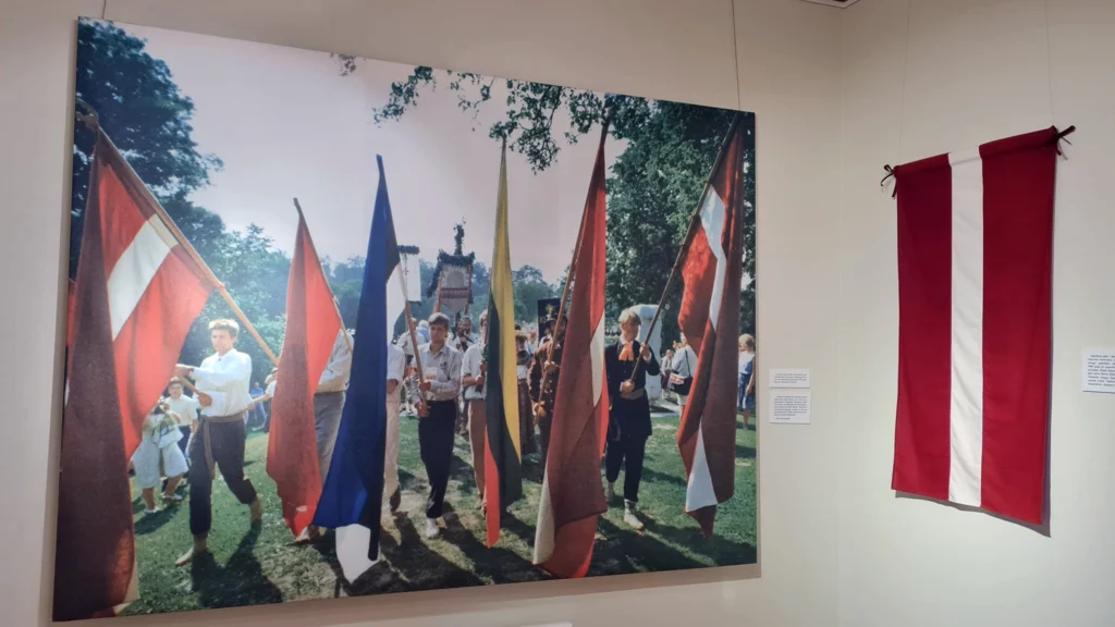 Izstāde “Brīvības ceļš”. Liela fotogrāfija, kur redzami cilvēki ar karogiem. Labajā pusē Latvijas karogs