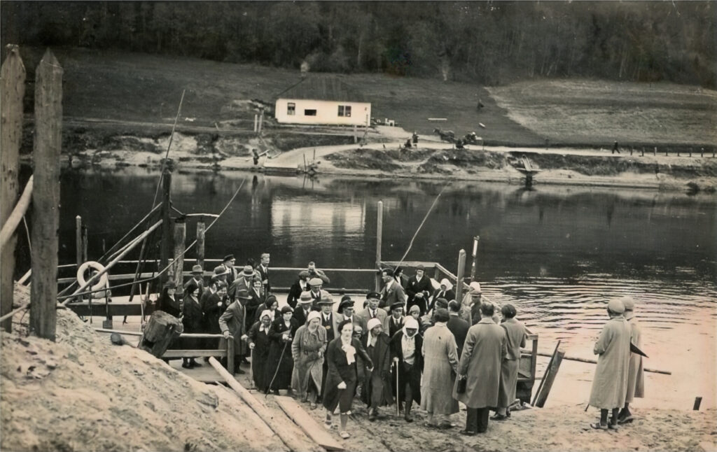 Prāmis jau jaunajā vietā - ap 600 m uz augšu no iepriekšējās. Atpūtnieki iekāpj Gaujas kreisajā krastā. Fotopastkarte , 20. gs. 30. gadi. Fotogrāfs nezināms